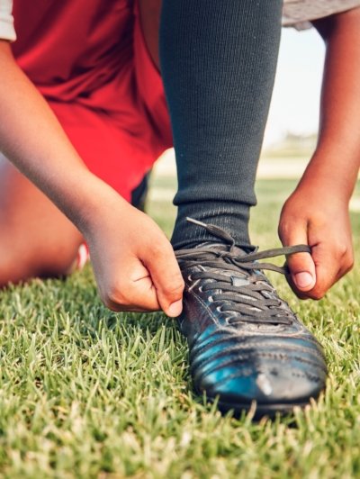 Sports, football field and child tie shoes for match workout, challenge contest or practice exercis